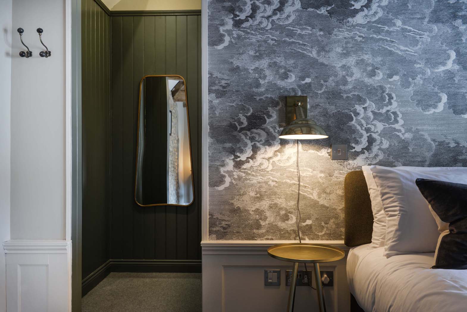 Litune - A peek through to the entrance of the room with brass light fixtures, dark green cladding and beautiful cloud wallpaper