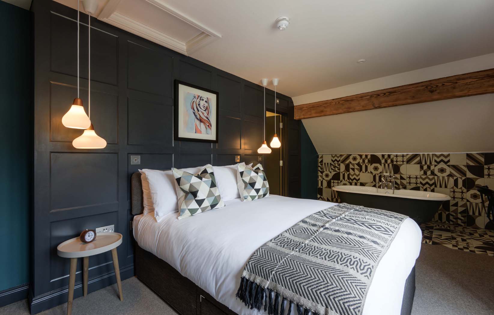 Watery Coombe - Romantic room painted in a dark palette with contrasting, crisp white bedlinen. A roll-top bath sits to the side of the room underneath an original wooden beam.